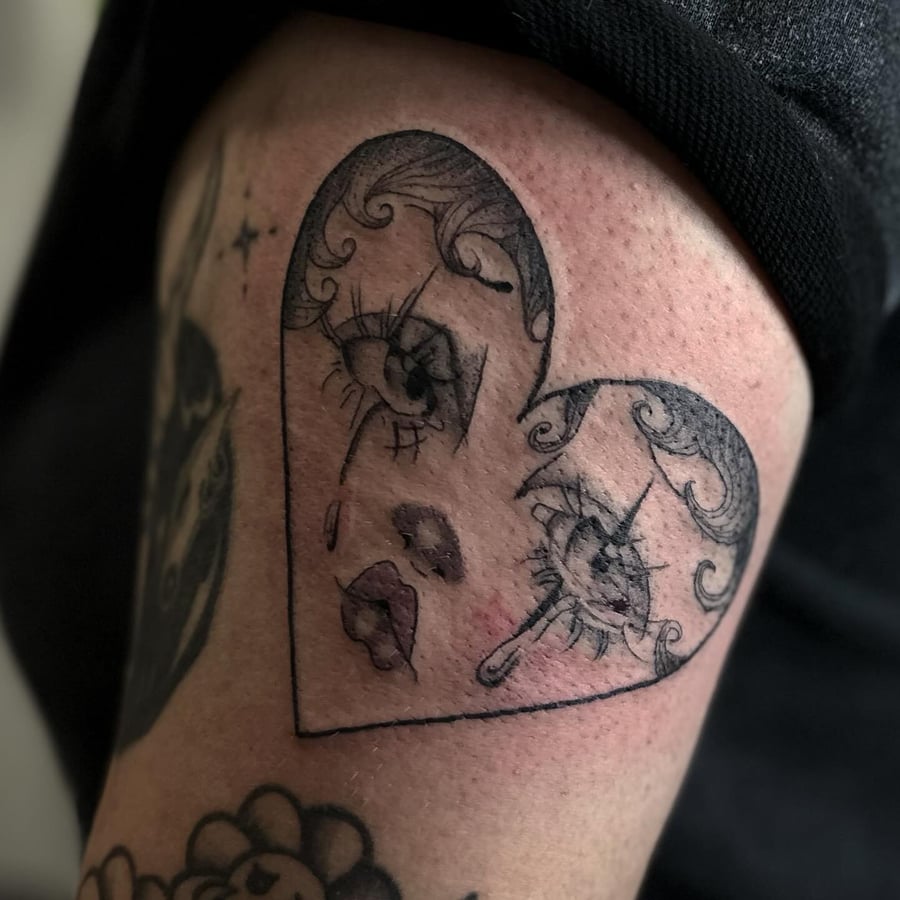 A black and grey heart-shaped design with crying eyes on the thigh, done in a fine line blackwork style — by Maddie Ramirez, los angeles