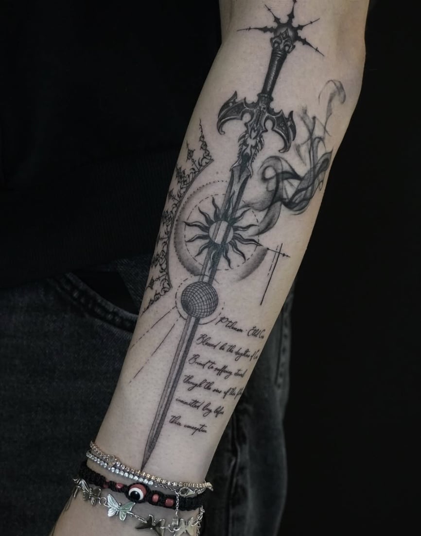A black and grey illustrative tattoo on the forearm featuring an ornate sword with intricate linework and accompanying script — by Jian Liang, los angeles