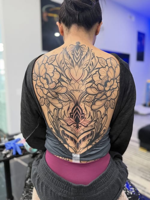 An intricate ornamental floral design in black and grey covering the full back with detailed linework and patterns — by zealous, los angeles