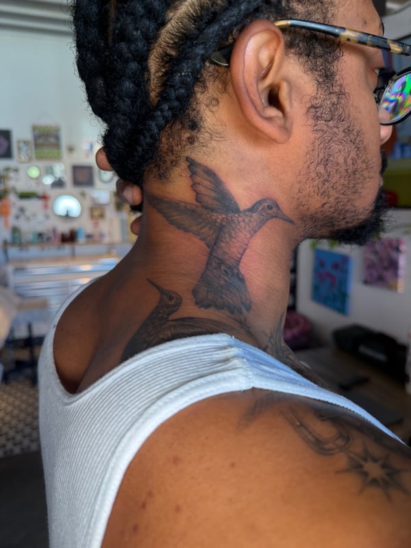 A realistic black and grey hummingbird tattoo on the neck, showcasing delicate details and shading — by Kiera Garvin, los angeles