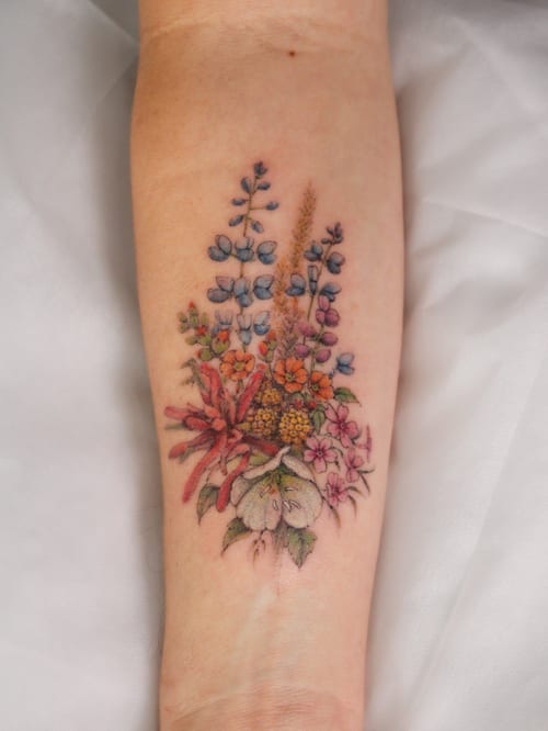 A colorful floral bouquet tattoo on the forearm with fine line details and a delicate, romantic style — by Melanie Benoit, los angeles