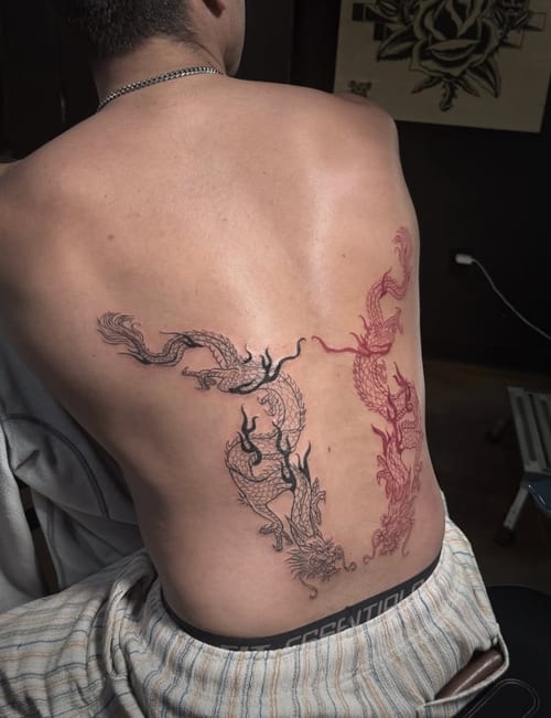 A large tattoo of two dragons on the back, featuring intricate black linework and red highlights in a Japanese style — by Shelby Bianco, los angeles