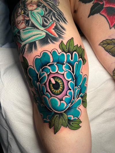 A colorful Neo-Traditional tattoo of an eye surrounded by floral elements on the knee, featuring bold outlines and vibrant colors — by Megan Rose, los angeles