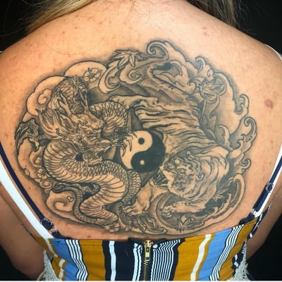 A bold black and grey tattoo of a dragon and tiger with a yin yang symbol on the back, featuring Japanese style elements — by Sandra Price, los angeles