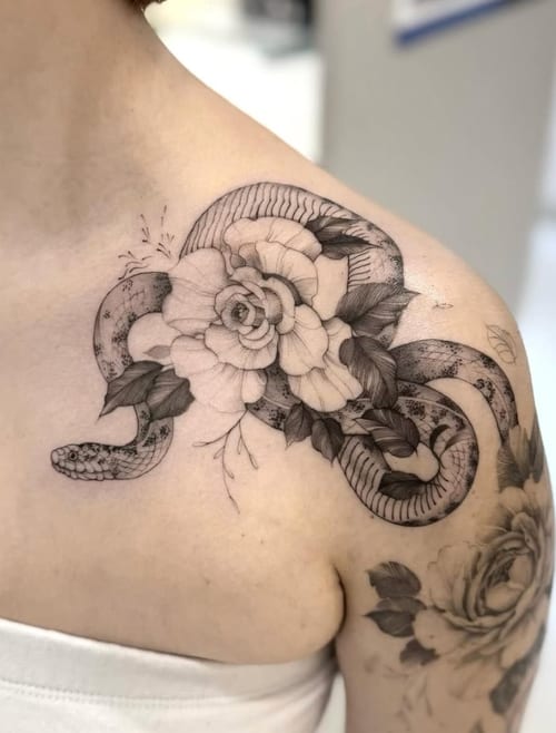 A black and grey tattoo on the shoulder featuring a detailed snake intertwined with a large flower, rendered in fine line and blackwork style — by otaybeatdown, los angeles