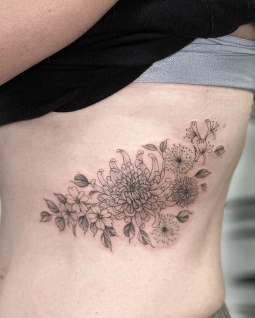 A delicate black and grey floral arrangement tattoo on the rib, featuring fine line work and intricate details — by Melanie Benoit, los angeles