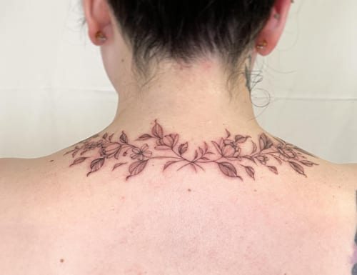 A delicate fine line floral garland tattoo on the neck, featuring detailed flowers and leaves in black and grey — by Melanie Benoit, los angeles