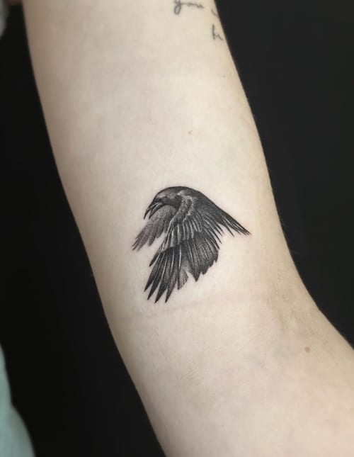 A minimalist blackwork tattoo of a bird in flight on the inner arm, featuring clean lines and simple shading — by Jian Liang, los angeles