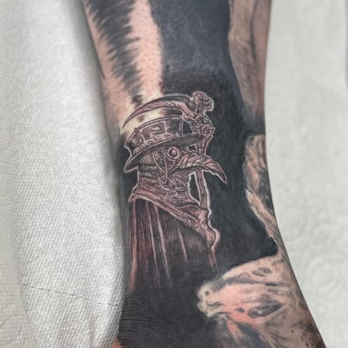 A detailed black and grey tattoo of a plague doctor on the forearm, featuring intricate linework and shading — by Sandra Price, los angeles