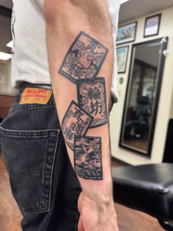 A bold black and grey tattoo of playing cards with script on the forearm, featuring a graphic illustrative style — by Sandra Price, ventura, ca