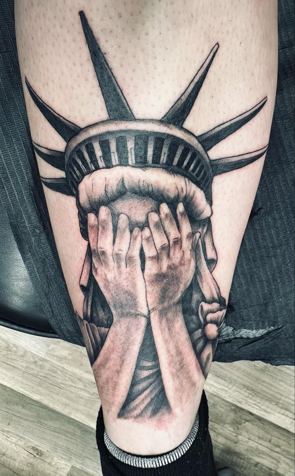 A black and grey realism tattoo of the Statue of Liberty covering its face, located on the calf with detailed shading — by Dretty, long beach, ca
