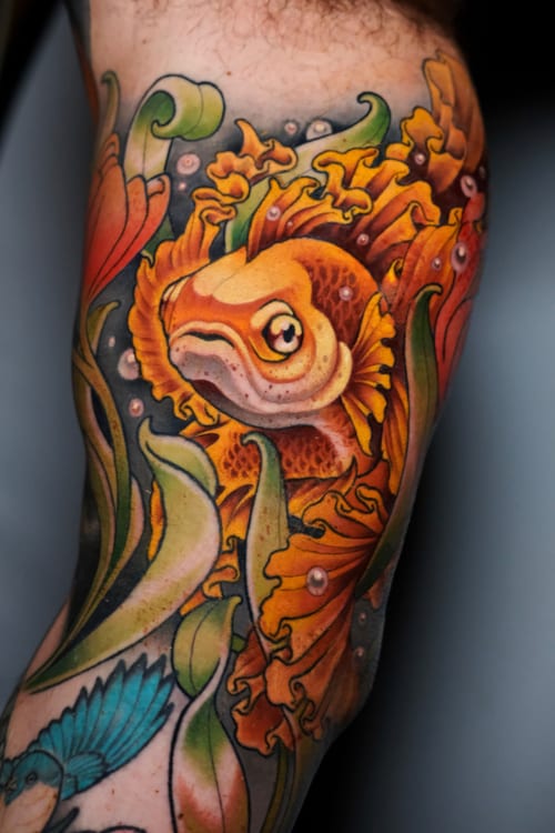 A vibrant color tattoo of a fish surrounded by floral elements on the arm, done in a Neo-Traditional style with bold outlines and rich colors — by Gabe Motta, los angeles
