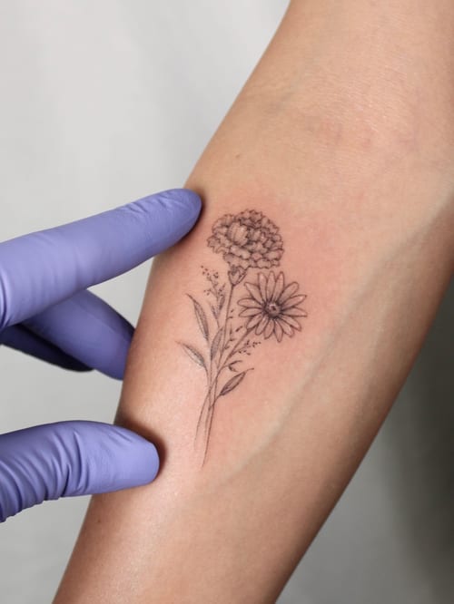 A delicate fine line floral tattoo on the forearm featuring a small bouquet in black and grey — by Melanie Benoit, los angeles