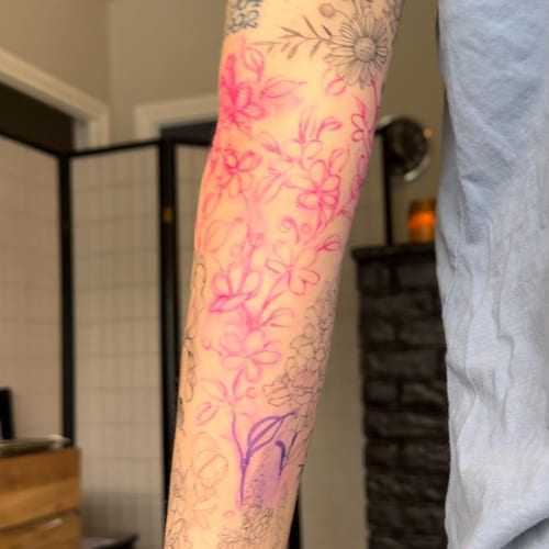 A delicate floral design with pink and black linework on the forearm, featuring various flowers — by Melanie Benoit, los angeles