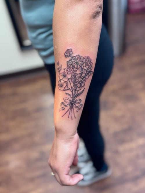 A delicate fine line black and grey bouquet of flowers tattooed on the forearm — by Sandra Price, los angeles