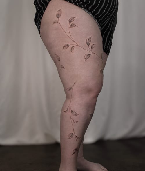 A delicate fine line vine with leaves tattoo on the leg, featuring a minimalist black and grey style — by Melanie Benoit, los angeles