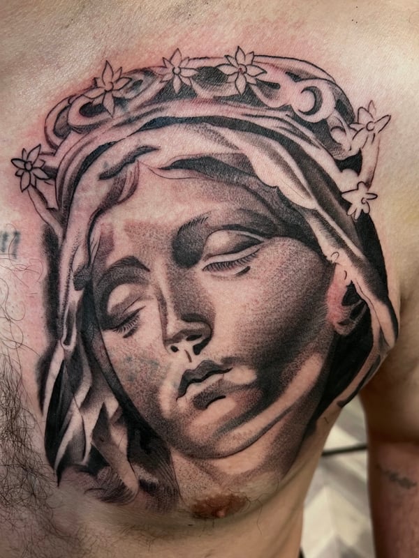 A realistic black and grey portrait of a religious figure on the chest, showcasing detailed shading and lifelike features — by Josue Bravo, los angeles