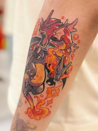 A colorful illustrative tattoo of two dragons with fiery elements on the forearm, featuring bold outlines and vibrant colors — by Tweetwee, los angeles