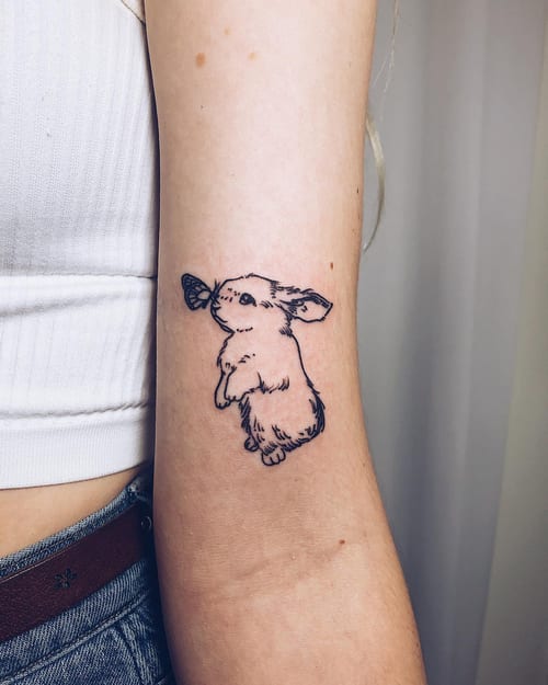A delicate black and grey linework tattoo of a rabbit with a butterfly on the arm, featuring a minimalist style — by Level tattoo, los angeles