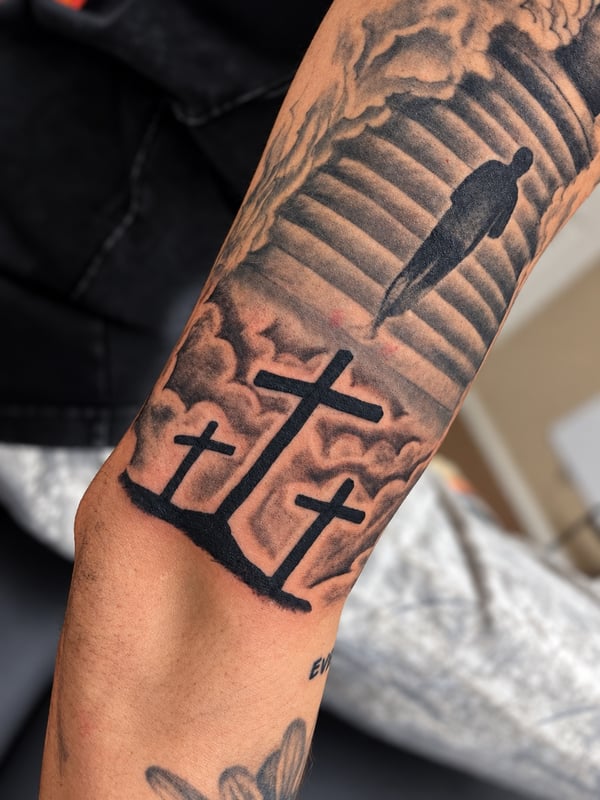 A black and grey tattoo on the forearm depicting three crosses and stairs leading to heaven, symbolizing a spiritual journey — by HEAVY INK, chino, ca