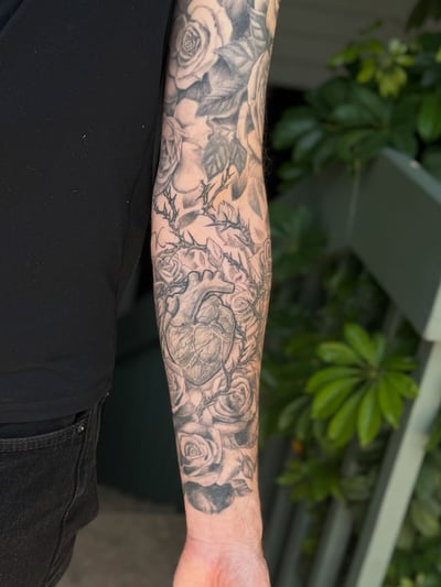 A black and grey tattoo of an anatomical heart surrounded by roses on the forearm, featuring realistic shading and detail — by Sandra Price, los angeles