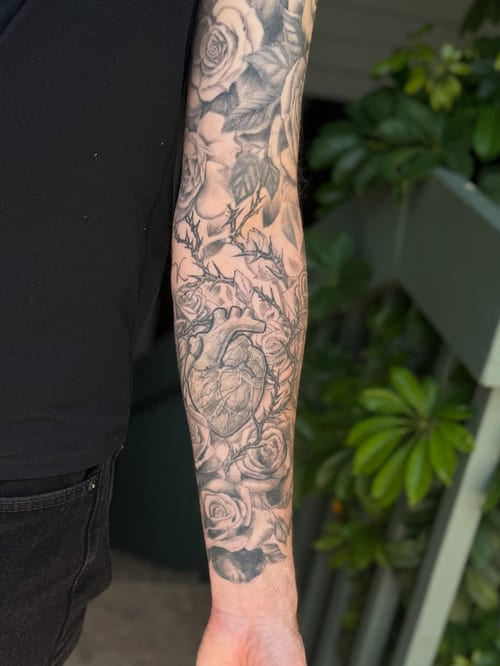 A black and grey tattoo of an anatomical heart surrounded by roses on the forearm, featuring realistic shading and detail — by Sandra Price, los angeles