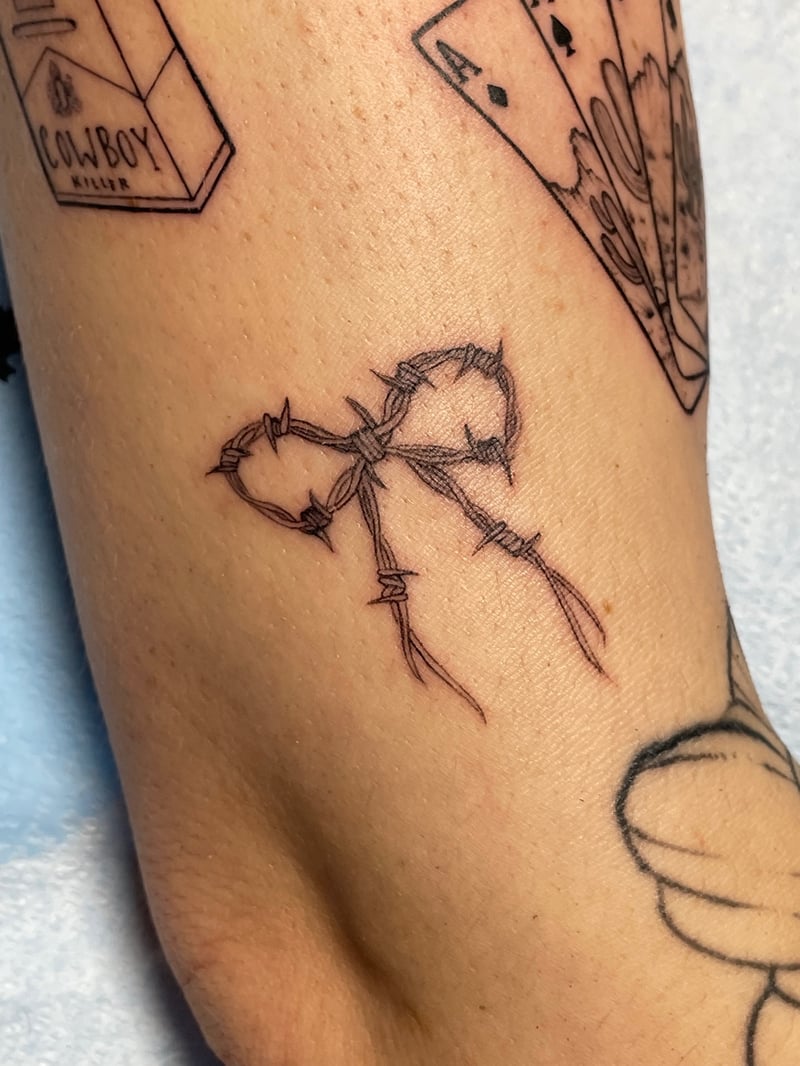 delicate fine-line tattoo of a bow tied from barbed wire and thorns by Vince Espinoza, a fine line tattoo artist in los angeles