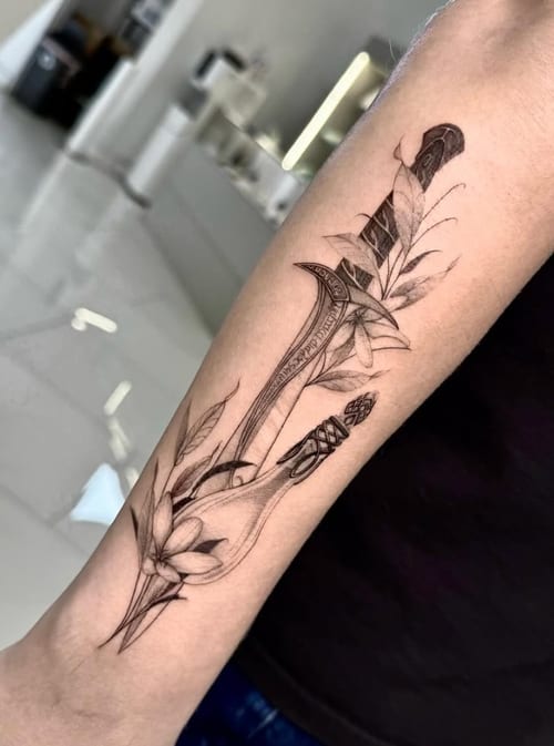 A fine line black and grey tattoo of a dagger intertwined with floral elements on the forearm, showcasing intricate details and delicate shading — by otaybeatdown, los angeles