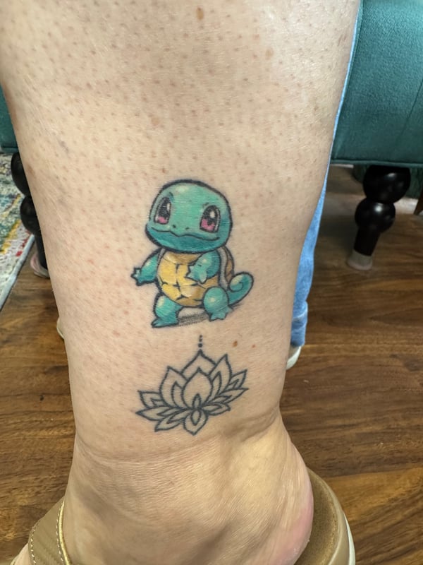 A colorful tattoo of Squirtle and a lotus flower on the calf, combining anime and floral elements — by Sandra Price, ventura, ca