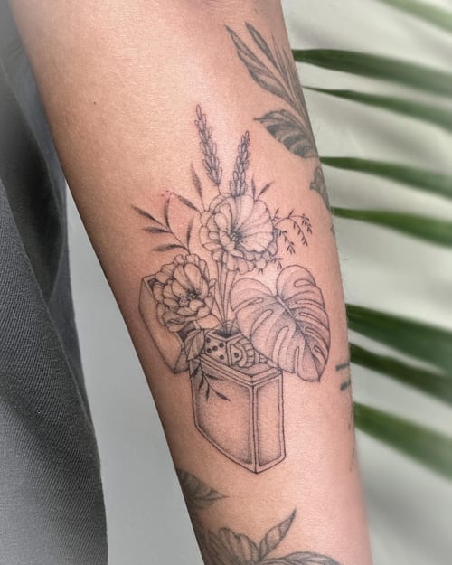 A delicate black and grey fine line tattoo of flowers emerging from a lighter on the forearm — by Melanie Benoit, los angeles