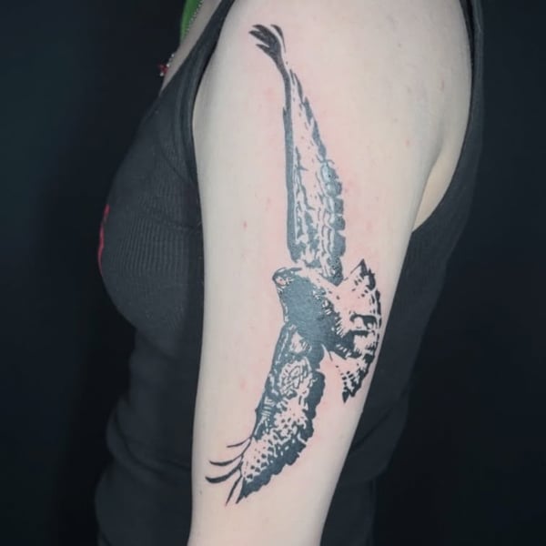 A bold blackwork tattoo of a flying bird on the upper arm, featuring strong illustrative lines — by Hannah , fountain valley, ca