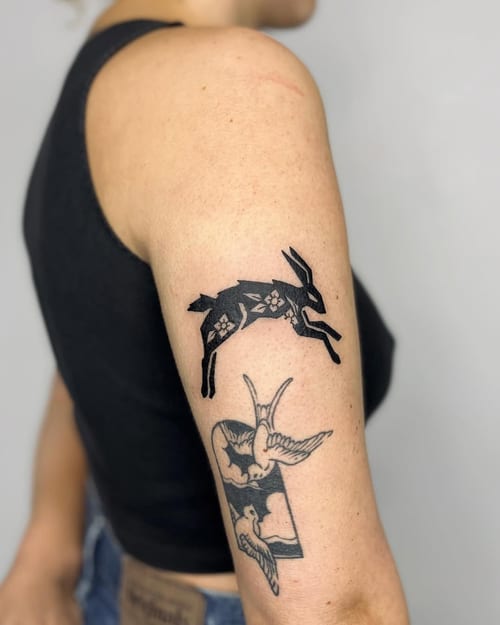 A bold blackwork tattoo of a rabbit and birds on the upper arm, featuring graphic and illustrative elements — by Dylan Aiello, los angeles