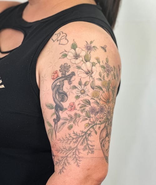 A colorful tattoo of a snake intertwined with a floral arrangement on the upper arm, featuring delicate flowers and detailed botanical elements — by Melanie Benoit, los angeles