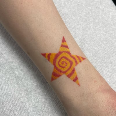 A bold and colorful star tattoo with a spiral design on the forearm, featuring vibrant red and yellow hues — by Sandra Price, los angeles