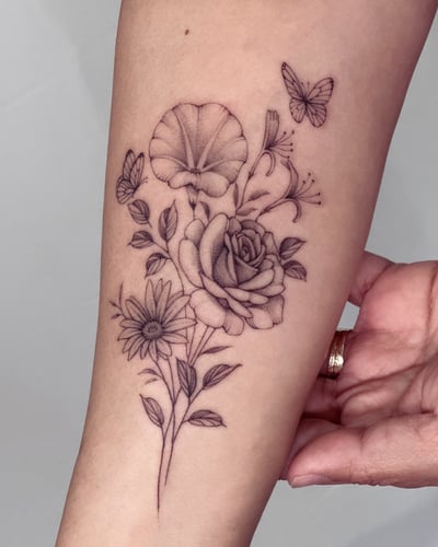 A delicate black and grey floral bouquet with butterflies on the forearm, featuring fine line roses and other flowers — by Melanie Benoit, los angeles
