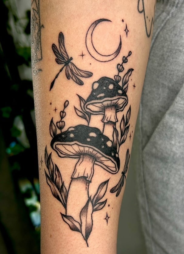 A black and grey tattoo on the forearm featuring two mushrooms, a crescent moon, and dragonflies with fine line details and blackwork style — by NJ TATTOOZ, los angeles