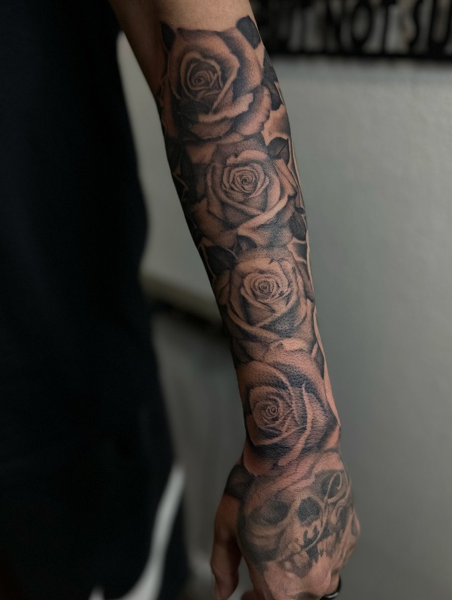 A bold black and grey floral sleeve tattoo with roses and a skull, covering the full sleeve — by Maddie Ramirez, los angeles