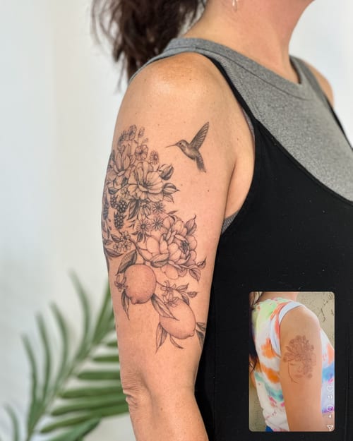 A delicate black and grey tattoo of a hummingbird and floral arrangement on the upper arm, featuring fine line details and intricate blackwork — by Melanie Benoit, los angeles