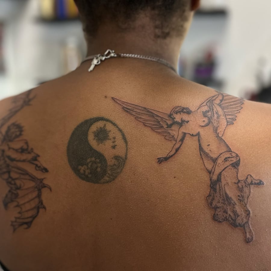 A black and grey yin yang tattoo with an angel and demon on the back, featuring fine line and dark art style — by Maddie Ramirez, los angeles