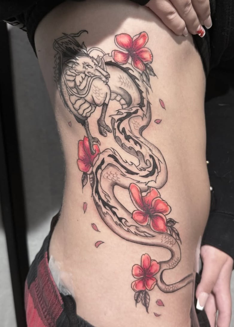 A mixed color tattoo of a Japanese-style dragon intertwined with red flowers on the rib, featuring detailed linework and shading — by Shelby Bianco, los angeles