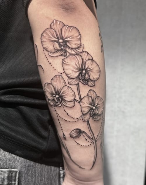 A fine line black and grey tattoo of orchids on the forearm, featuring delicate floral details and subtle shading — by Shelby Bianco, los angeles