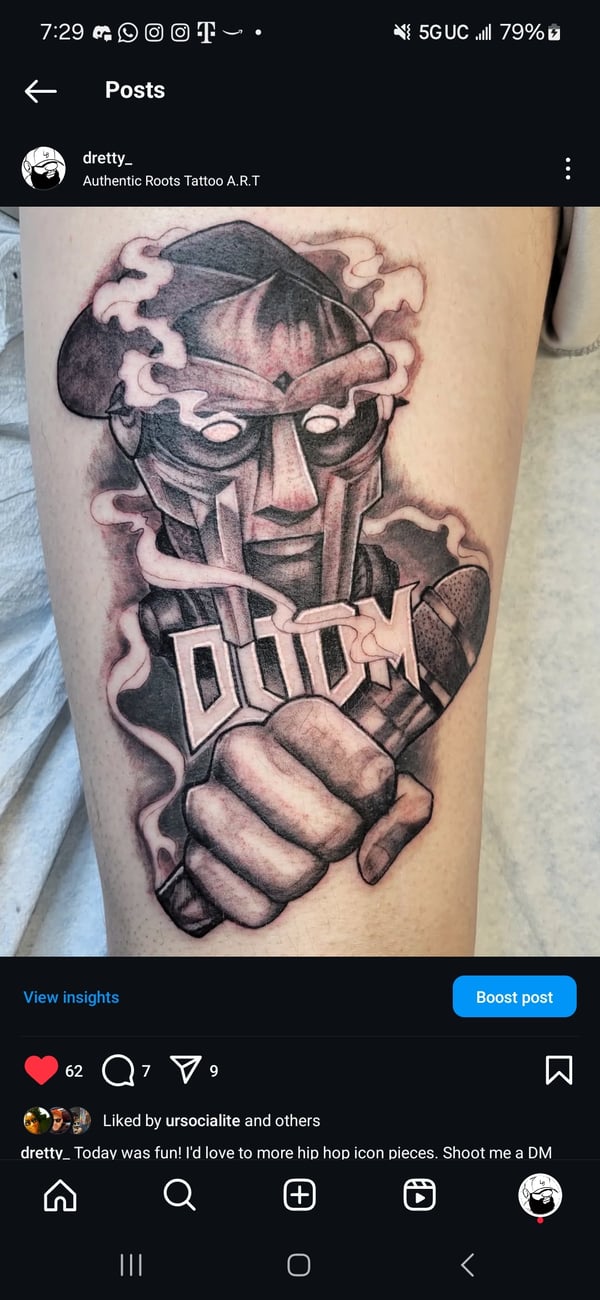A black and grey illustrative tattoo of MF DOOM on the thigh, featuring bold lines and shading — by Dretty, long beach, ca