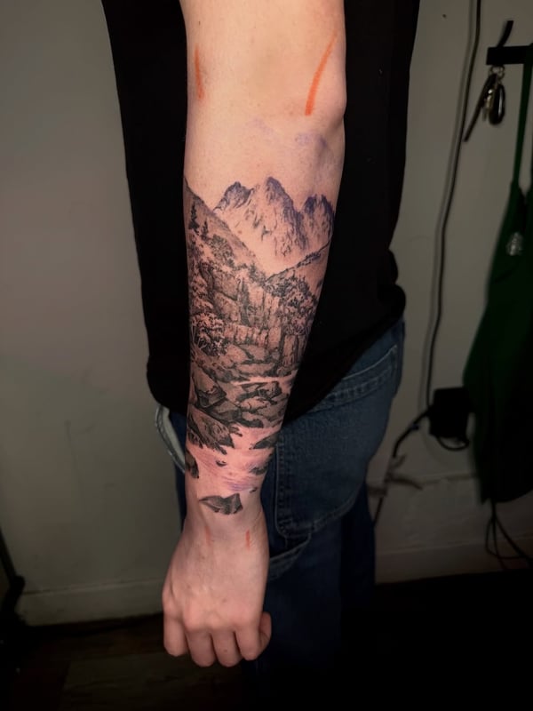 A detailed black and grey mountain landscape tattoo on the forearm with realistic shading and texture — by zealous, los angeles