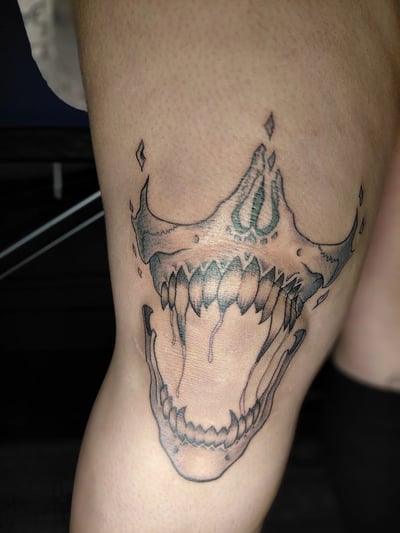 A black and grey linework tattoo of a stylized skull with an open mouth on the thigh, featuring sharp teeth and abstract elements — by anoetic.designs.ultd, los angeles