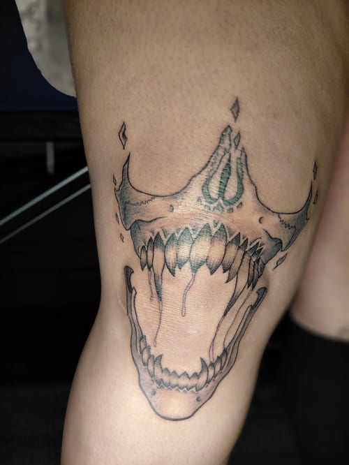 A black and grey linework tattoo of a stylized skull with an open mouth on the thigh, featuring sharp teeth and abstract elements — by anoetic.designs.ultd, los angeles