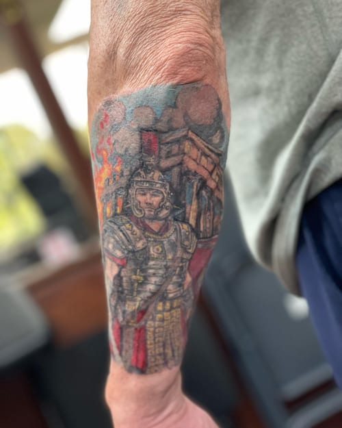A colorful illustrative tattoo of a Roman soldier on the forearm, featuring detailed armor and a historical setting — by Sandra Price, los angeles