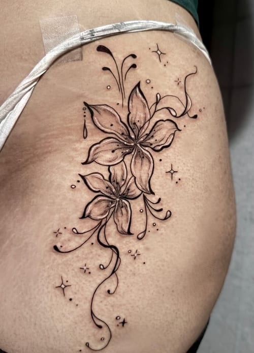 A black and grey fine line floral tattoo on the hip, featuring two detailed flowers with delicate linework and decorative elements — by Shelby Bianco, los angeles