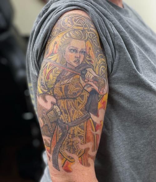 A colorful Celtic warrior woman tattoo on the upper arm, featuring intricate knotwork and a bold illustrative style — by Sandra Price, los angeles