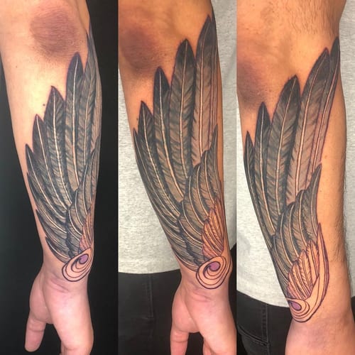 A bold black and grey wing tattoo on the forearm with detailed feather design — by Sandra Price, los angeles