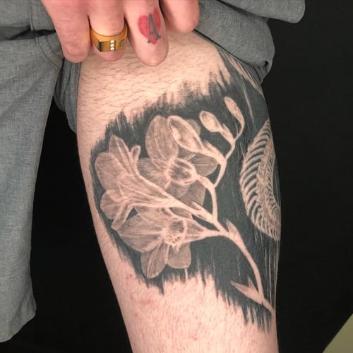 A bold black and grey flower tattoo on the thigh with a striking blackwork background — by Sandra Price, los angeles